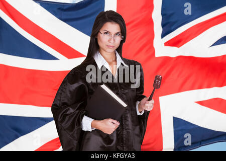 Portrait Of Female Judge With Book And Gavel Standing In Front Of Uk Flag Stock Photo