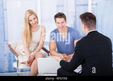 Financial advisor explaining investment plan to young couple on laptop in office Stock Photo