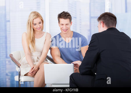 Financial advisor explaining investment plan to young couple on laptop in office Stock Photo