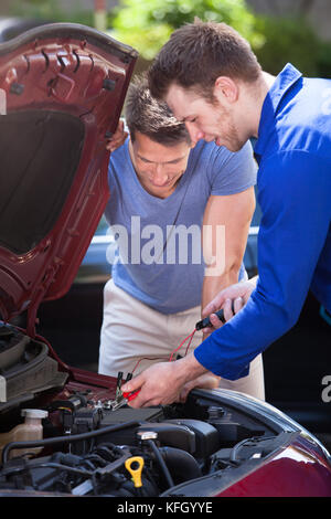 Male car owner with mechanic testing car battery outdoors Stock Photo