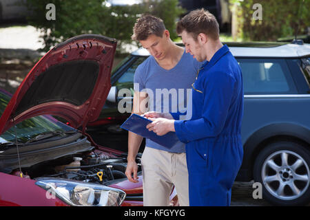 Young mechanic showing clipboard to customer by breakdown car Stock Photo