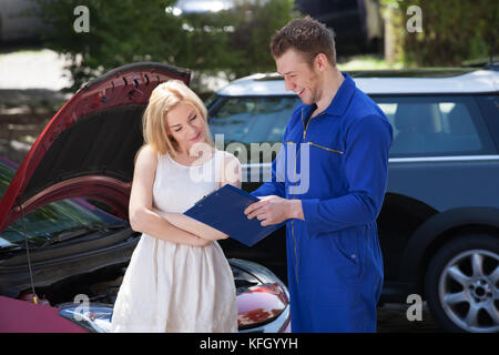 Young mechanic showing clipboard to female customer by breakdown car Stock Photo
