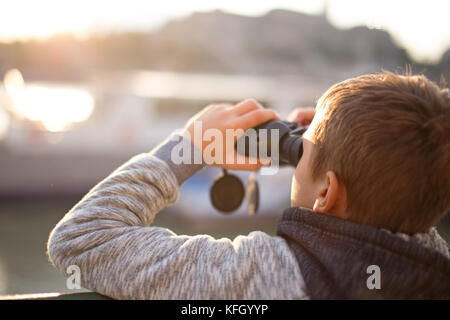 Little caucasian boy watching, looking, searching, gazing by binoculars in sunset Stock Photo