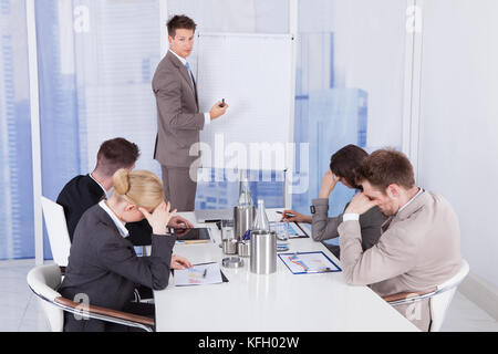 Colleagues getting bored during business presentation given by businessman in office Stock Photo