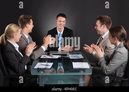 Young business people applauding for male colleague after presentation against black background Stock Photo