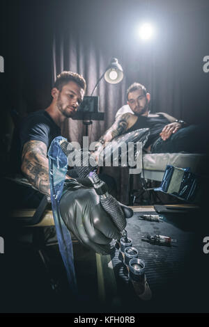 Portrait of a man tattoo master showing a process of tattoo creation in a man's hand under the lamplight Stock Photo