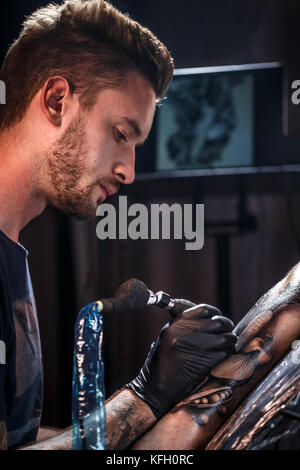 Professional tattoo artist makes a tattoo on a young man's hand Stock Photo