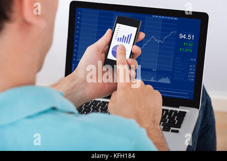 Cropped image of man analyzing stock market using smartphone and laptop at home Stock Photo