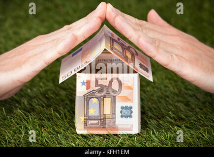Businessman's hands protecting house made of euro notes on grassy land Stock Photo