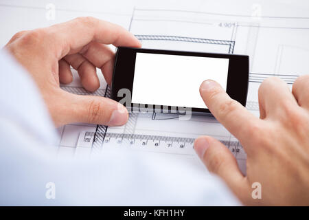 Closeup of architect touching smartphone's screen over blueprint in office Stock Photo