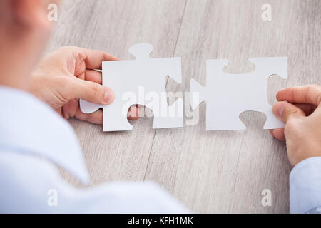 Cropped image of businessman joining jigsaw pieces at desk Stock Photo