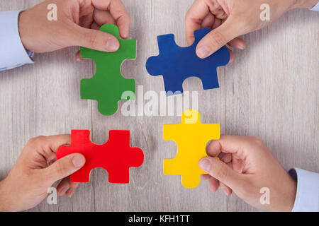 Cropped image of businesspeople joining multicolored puzzle pieces at desk in office Stock Photo