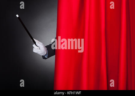 Cropped image of magician holding wand behind stage curtain Stock Photo