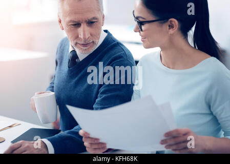 Mature businessman looking at papers brought by young employee Stock Photo