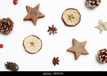 Christmas festive styled stock image composition. Decorative pattern. Pine cones, red berries, dried apple fruit, anise and wooden stars isolated on white wooden background. Flat lay, top view. Stock Photo