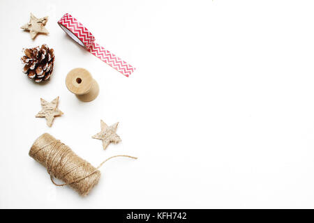 Christmas festive styled stock image composition. Pinecone, decorative tape, ribbon, rope, berries, anise and wooden stars isolated on white wooden background. Gift wrapping. Flat lay, top view. Stock Photo