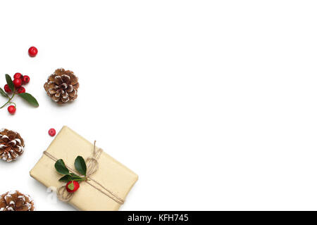 Christmas festive styled stock image composition. Handmade gift box, red berries and pine cones isolated on white wooden background. Flat lay, top view. Stock Photo