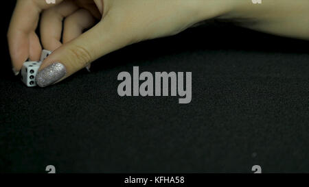 Detail of dice on black table. Female hand picks two dice from the table. Close up. Stock Photo