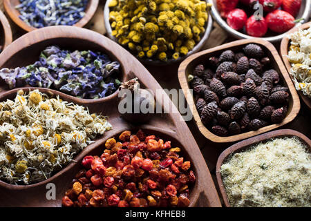 Natural medicine. Herbs, berries and flowers in bowls on wooden table. Stock Photo