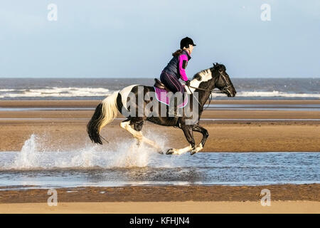 Southport, Merseyside, UK. 29th October 2017. UK Weather: A beautiful sunny start to the day as Yvonne Allen canters her 7 year old horse 'Trev' through the tide on the golden sands of Southport beach in Merseyside.  Credit: Cernan Elias/Alamy Live News Stock Photo