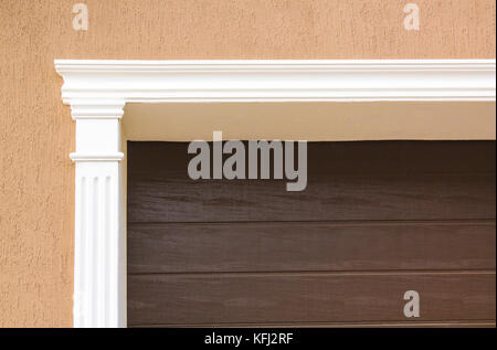 The brown metal garage door is decorated with a white arch of stucco for the background. Stock Photo