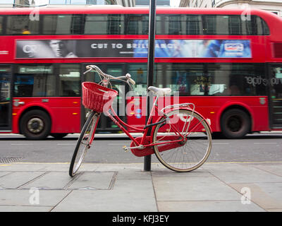 An elegant lady's red bicycle chained to a lampost in central London as a bus travels past in the background Stock Photo