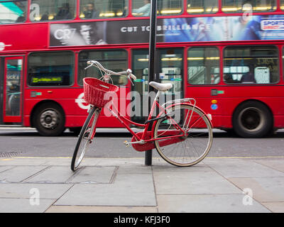 An elegant lady's red bicycle chained to a lampost in central London as a bus travels past in the background Stock Photo