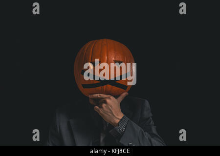 Man with a pumpkin head dressed in a suit against a black background Stock Photo