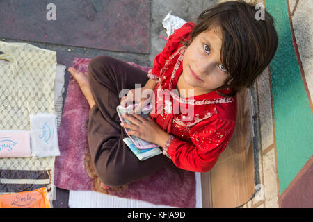 Tehran, IRAN - August 16, 2017 A little girl with red shirt selling small tissue packages at street pavement, top view Stock Photo
