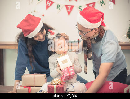 Happy family Asia family wear santa claus hat unwrap Christmas gift box at house xmas party,Holiday celebrating festive concept,vintage filter Stock Photo