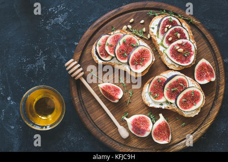 Fresh fig and goat cheese bruschetta set topped with pine nuts, honey and thyme. Gourmet appetizer, healthy snack or breakfast. Top view, toned image Stock Photo