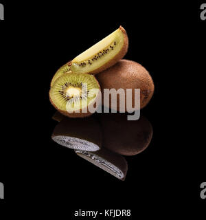 Bunch of whole kiwi fruit and in a cut isolated on black glossy background with real reflection. Stock Photo