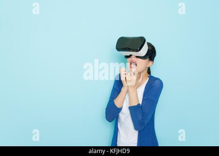 beautiful young girl wearing lifestyle clothing viewing VR device 3d image video and standing in blue background feeling terrible. Stock Photo