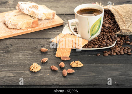 Healthy snack with slices of pound cake,  biscuits, almonds, walnuts and a cup of coffee on a plate covered with coffee beans Stock Photo