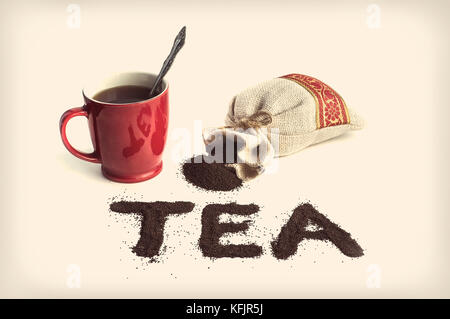 The word tea is written with a granular black tea on the table on a white background. Mug and tea packaging Stock Photo