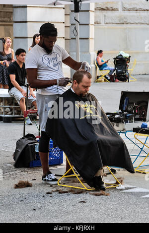 African American Barber cuts for free white poor in the courtyard of  City Hall, Philadelphia, Pennsylvania, USA Stock Photo