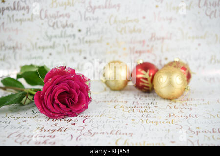Christmas photography image with glitter red rose flower and red gold sparkly xmas bauble tree decorations on white shiny wrapping paper background Stock Photo