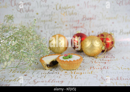 Christmas food photography image with glitter flowers red gold baubles and iced mince pies on white shiny festive writing wrapping paper background Stock Photo