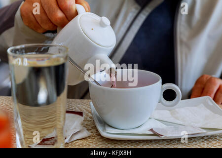 Hands holding a glass brewer in one hand and a cup of tea in another. Hands pouring Stock Photo