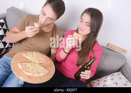 Beautiful young couple drinking beer and eating pizza. Indoors. Stock Photo
