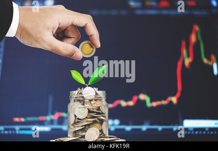 Investment in online stock market concept, Hand putting coin in glass jar with increasing money and plant glowing up Stock Photo