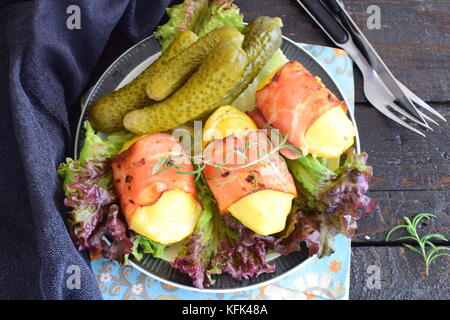 Oven cooked potato with cheese wrapped in bacon, served with pickled vegetables. Stock Photo