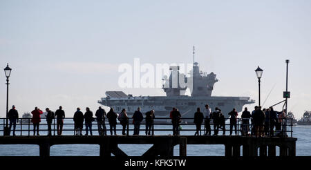 People watch as the 65,000-tonne HMS Queen Elizabeth, the UK's newest aircraft carrier, departs from Portsmouth Naval Base, the carrier is due to spend a month at sea around the south-west of the United Kingdom testing out its radar, communications and other technical equipment. Stock Photo