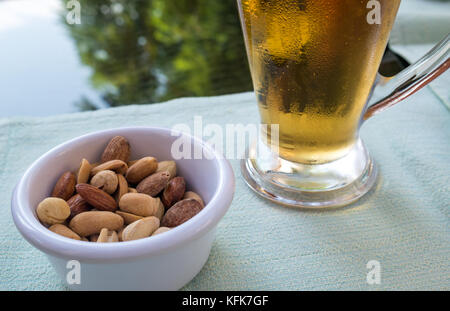 Close up of cold beer glass mug and mixed nuts in small dish on lunch table setting with blurred background, Jordan, Middle East Stock Photo