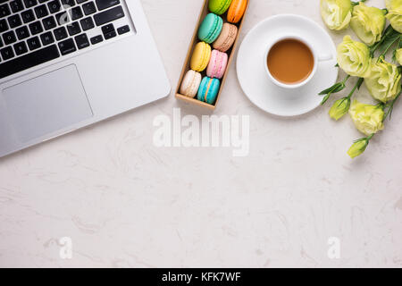 White desk with colorful macaroons, flowers, notebook, laptop and cup of coffee Stock Photo