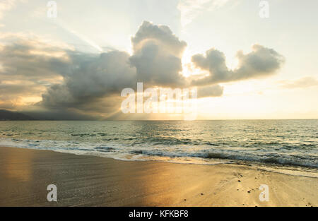 Sunset ocean is a serene scenic seascape on the beach with the bright sun setting on the ocean horizon as water rushes to the shore. Stock Photo