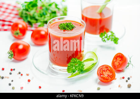 red tomato juice in transparent glasses with parsley, cutted tomato fruit, cucumber and dry pepper, close up Stock Photo