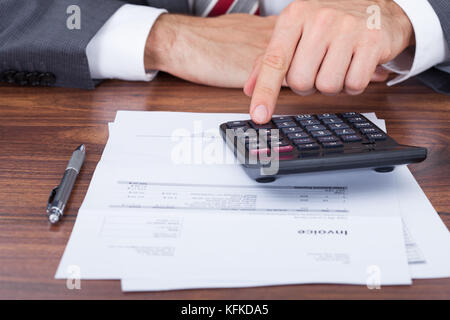Midsection of businessman using calculator on invoice documents at office desk Stock Photo
