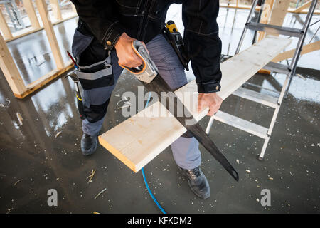 Low Section Of Carpenter Using Hand Saw To Cut Plank Stock Photo