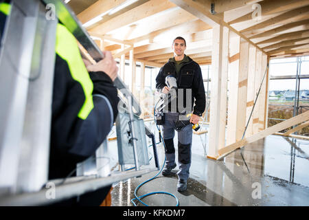 Carpenter Smiling While Female Colleague Carrying Ladder At Site Stock Photo
